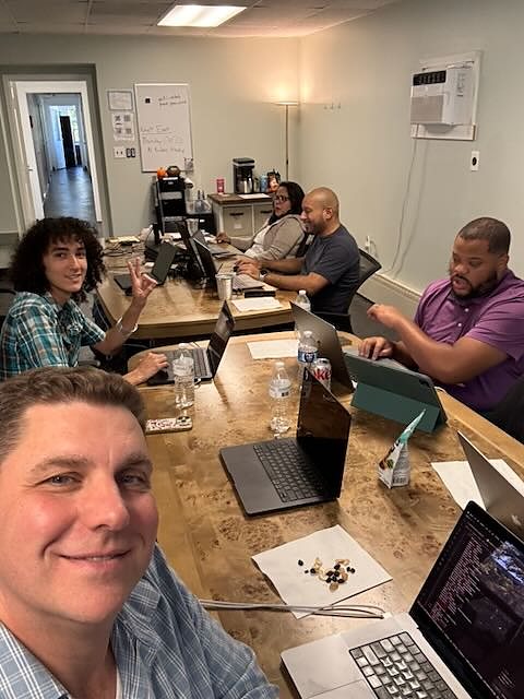 Five people coworking on laptops at a long table